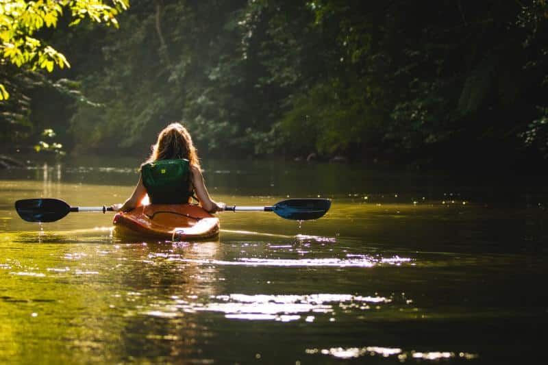 woman kayaking in a stream facing away from the camera