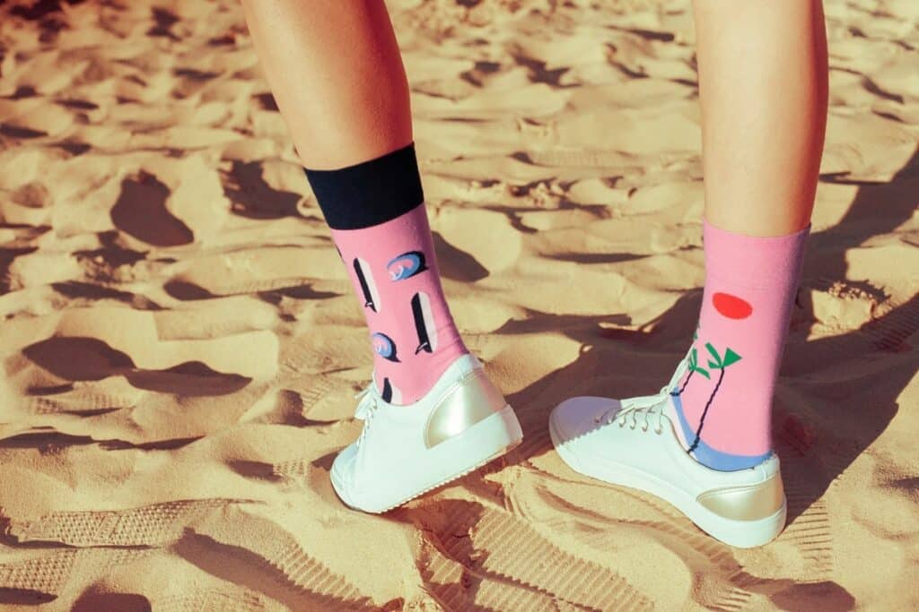 someone wearing a pear of pink custom socks and white tennis shoes, walking on a beach.