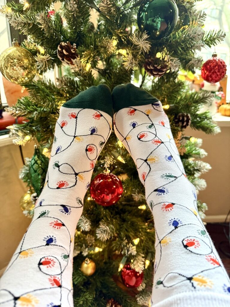 person wearing a pair of socks with christmas lights design in front of a christmas tree