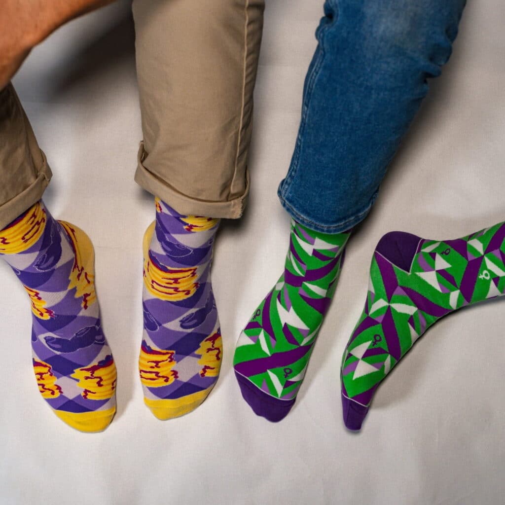 two pairs of promotional socks, purple with orange pattern on the left, purple with green pattern on the right