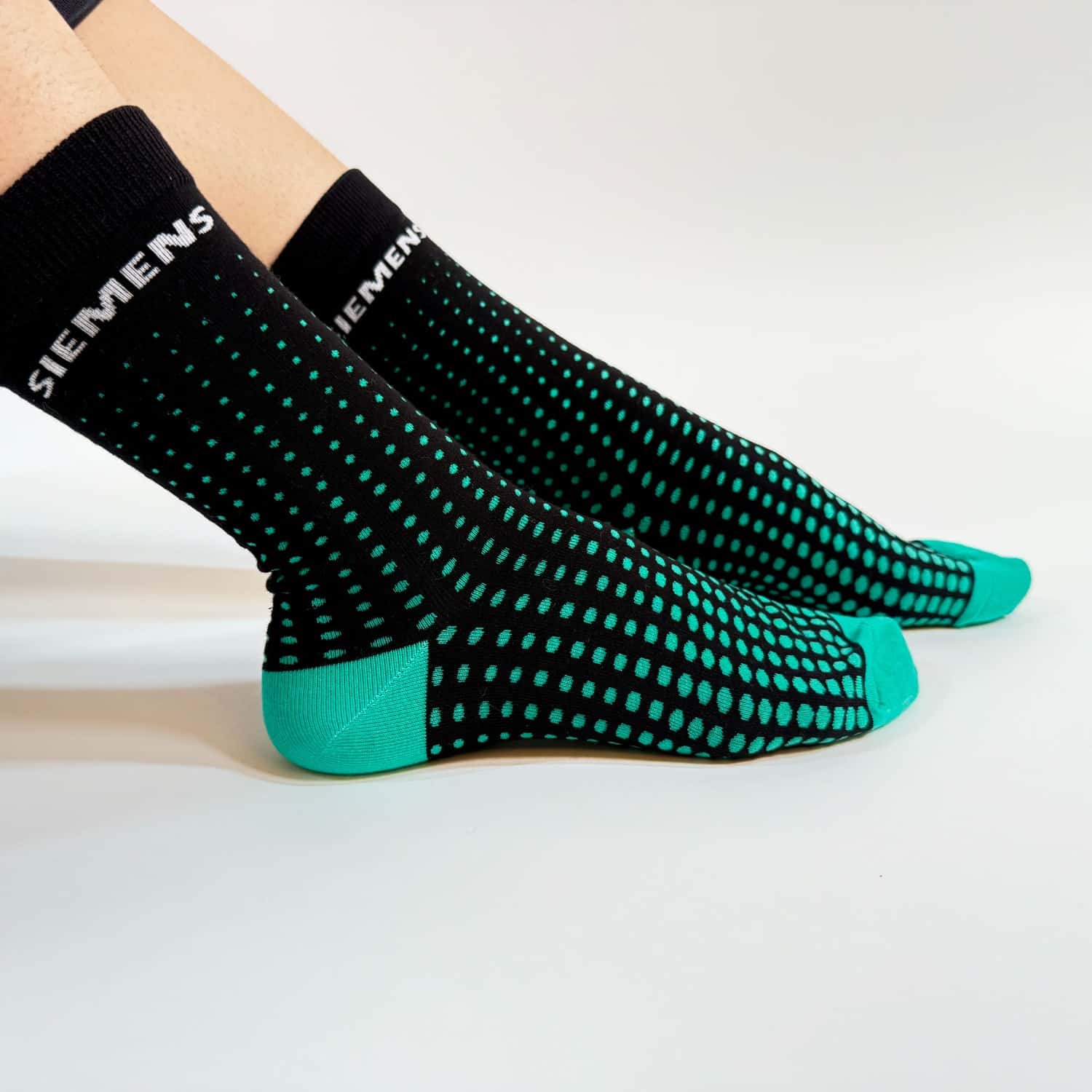 custom branded socks from spirit sox usa, featuring a black background, geometric teal gradient pattern, and teal sole and tips with white brand name around the cuff