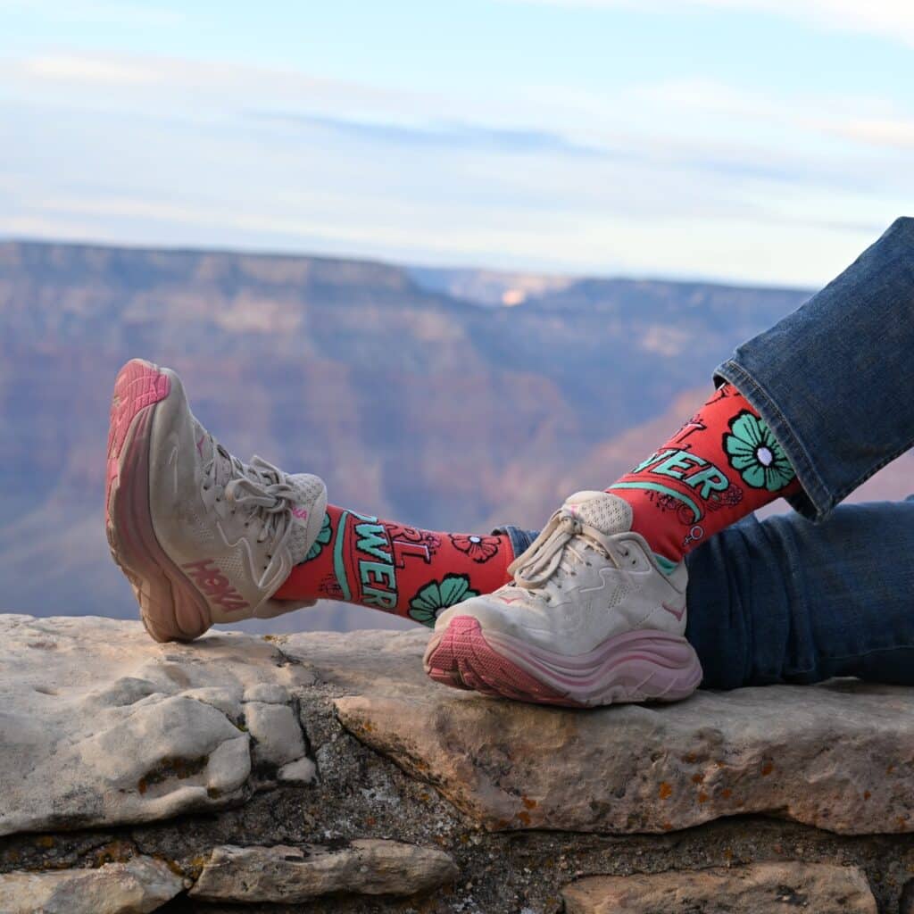 a mockup image of a branded corporate sock with flamingo base color and cyan letter and flower design