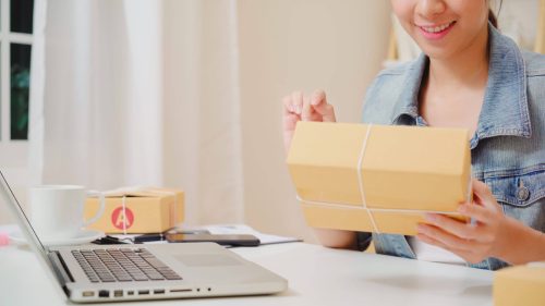 woman with package checking product inventory on in-home laptop computer